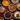 A top-down view of a collection of various pies arranged on a dark wooden surface. The pies include pumpkin, pecan, apple, and cranberry, along with other assortments. Scattered around the pies are autumn leaves, small pumpkins, pine cones, and bundles of cinnamon sticks, evoking a warm, autumnal, and festive holiday atmosphere.