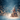 A richly decorated Christmas tree, glowing with warm golden lights and festive ornaments in red, blue, and gold, stands prominently on a shimmering, glitter-covered surface. Delicate white snowflakes fall from a deep blue, soft-focus background filled with warm, golden bokeh lights, creating an enchanting and magical winter wonderland scene.