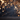 A festive background image featuring bright golden sparklers and shimmering bokeh lights. Decorative golden Christmas tree branches adorned with glittery stars and curled ribbons frame the top. The scene is set against a dark, moody background with a glittery dark foreground, creating a magical and elegant atmosphere with prominent warm golden tones.