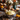 A close-up shot showcases a bowl of fluffy mashed potatoes, topped with a sprig of fresh herbs, sitting on a wooden table amidst a festive Thanksgiving spread. Miniature pumpkins, candles, and floral arrangements add to the warm, autumnal ambiance. The bowl has a white base with an intricate blue floral design along the rim.