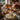 A close-up shot of a Thanksgiving dinner table. In the foreground, a bowl of mashed potatoes topped with herbs sits on a wooden table next to a gray linen cloth. In the blurred background are a roasted turkey, other dishes, gourds, and lit candles, all contributing to a warm and inviting festive atmosphere.
