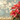 A vibrant red poinsettia plant is prominently featured on the right side of the frame, showcasing its distinct red bracts and green foliage. A layer of sparkling golden glitter covers the bottom foreground, while the background consists of soft, blurred light blue hues illuminated by numerous warm, circular golden bokeh lights, creating a festive and inviting atmosphere.