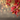 A close-up shot of vibrant red poinsettia flowers and glittery gold leaves positioned in the upper right corner of the frame. A cluster of small red berries hangs below the flowers on a delicate stem. The background is softly blurred with warm, shimmering golden and reddish bokeh lights, creating an elegant and festive holiday atmosphere.