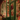 A charming vintage-style storefront painted deep green, adorned abundantly with twinkling warm white Christmas lights, evergreen garlands, and vibrant red berries. A festive red wreath hangs on the distressed wooden door, and the large display windows reveal more glowing lights and holiday decorations inside, creating a magical nighttime scene.