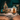 A charming light-colored brick house at night during winter, covered in snow and adorned with festive Christmas decorations. A large evergreen tree on the left is illuminated with multi-colored lights, while the front door of the house is decorated with green garlands, red poinsettias, and outlined with warm white lights, creating a cozy and inviting scene.