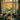 Five friends are seated around a low table in a warmly lit living room, enjoying food and conversation. A large window behind them offers a view of trees with bright yellow leaves, indicating it's autumn. The scene evokes a sense of warmth, friendship, and shared moments in a comfortable indoor setting.