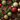 An overhead, full-frame view of a dense Christmas decoration arrangement. The image is filled with green evergreen branches, various red, gold, and lime green spherical ornaments, brown pine cones, and clusters of small red berries. The ornaments feature a mix of glittery, smooth matte, and textured styles, creating a rich and vibrant festive composition.