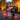 A vertical shot of two smiling children, a girl in a pink spiderweb dress and a boy in a skeleton costume, running down a paved street at dusk. They are holding orange pumpkin candy buckets, with a background of glowing warm string lights on autumn trees and a house, creating a magical Halloween scene.