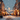 A vertical photo depicting a snow-covered city street at night, beautifully lit by numerous warm, golden Christmas lights. Softly falling snow creates a bokeh effect throughout the scene, contrasting with the cool blue-gray tones of the sky and the white snow on the ground. Buildings and decorated trees line both sides of the street, blurred into the background, adding to the overall atmospheric and enchanting winter scene.