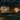 A modern, single-story cabin with dark wooden siding and large glass windows sits within a dense, dark forest at night. The windows glow warmly with intricate white and gold abstract floral patterns, reflecting the interior light. A stone path winds through a moonlit meadow of small white flowers, leading to the cabin, with spherical ground lamps providing additional soft illumination.
