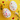 A vibrant flat lay image showcasing two white, decorative eggs adorned with numerous small, multi-colored hearts. They are arranged diagonally on a bright yellow background, which is also sprinkled with smaller heart-shaped confetti in various colors. A yellow flower with green leaves is positioned in the top left corner, and a white daisy-like flower with green foliage is in the bottom right, adding natural accents to this cheerful, festive composition.