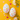 A flat lay image presents two white Easter eggs, each intricately decorated with a lively pattern of small, hand-painted hearts in various bright colors like pink, orange, yellow, and blue. These charming eggs rest on a vivid yellow surface, surrounded by an array of small paper heart cutouts in matching pastel tones and a sprig of white spring flowers with green leaves. The overall scene is bright and cheerful, conveying themes of love, spring, and holiday celebration.