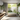 A beautifully lit modern bathroom showcasing a biophilic design, featuring gray concrete walls, a wooden floating vanity with a white vessel sink, and a freestanding white bathtub. A large window offers a view of a lush outdoor garden with a small plunge pool, while various green potted and cascading plants adorn the indoor space, creating a serene and luxurious atmosphere with natural light streaming in.