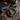 A top-down view showcases a slice of pumpkin pie on a blue-grey plate with a fork and knife. The pie sits on a distressed wooden table decorated with fallen maple leaves, pine cones, small pumpkins, and a wooden tray with gourds. The composition creates a warm, autumnal scene.