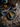 A top-down view showcases a slice of pumpkin pie on a blue-grey plate with a fork and knife. The pie sits on a distressed wooden table decorated with fallen maple leaves, pine cones, small pumpkins, and a wooden tray with gourds. The composition creates a warm, autumnal scene.