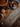 Overhead view of a Thanksgiving arrangement. A whole pumpkin pie and a slice of pie on a plate are displayed on a dark wooden surface. A small pumpkin, burlap, acorns, and scattered autumn leaves complete the festive scene.