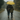 A couple is depicted from behind, walking away from the viewer on a wet, paved country road during a gentle rain. They share a bright yellow umbrella, and the man has his arm around the woman's shoulder. The scene conveys intimacy and togetherness, with lush, muted green and brown trees lining the road under an overcast sky.