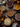 A top-down view displays a variety of pies on a dark, rustic wooden table. The pies include apple, pecan, cranberry, chocolate, and pumpkin, each with distinct crusts and fillings. Decorative elements such as small pumpkins, gourds, autumn leaves, and pinecones are scattered amongst the pies, creating a warm and inviting autumn-themed scene.
