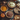A high-angle shot captures a festive Thanksgiving dessert display. Several pies including pumpkin, pecan, apple, and a cream-topped pie sit on metal plates atop a dark, textured surface. Decorative gourds, pinecones, nuts, and fall foliage surround the pies, with a vintage-style teapot peeking from the background.