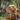 A painting depicting a young blonde woman in profile, wearing stylish gold-framed sunglasses and a dark floral dress, blowing a stream of iridescent soap bubbles into the air. She is seated on green grass at a sunny outdoor picnic, with a white blanket, bottles of red soda, and a picnic basket visible. In the blurred background, other people are also enjoying the park under dappled sunlight filtering through green trees, creating a lively and cheerful summer scene.