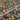 An expansive aerial view of a suburban neighborhood vibrant with autumn colors. Numerous single-family homes with diverse roof styles and light-colored walls are nestled among intensely red, orange, and yellow trees, interspersed with green lawns and evergreen foliage. Grey paved streets weave through the orderly residential landscape under bright daylight, conveying a sense of an established and picturesque community.