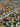 An expansive aerial view of a suburban neighborhood vibrant with autumn colors. Numerous single-family homes with diverse roof styles and light-colored walls are nestled among intensely red, orange, and yellow trees, interspersed with green lawns and evergreen foliage. Grey paved streets weave through the orderly residential landscape under bright daylight, conveying a sense of an established and picturesque community.