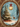 A richly detailed digital painting depicting a magical Christmas scene enclosed within an elaborate, gold, oval frame. A snow-covered evergreen tree, adorned with red ornaments and lit candles, stands beside a brown deer in a snowy forest, with numerous wrapped gifts at its base. A large, glowing gold and white ornament hangs from a red ribbon in the upper right, complementing the cool blue and white winter landscape with warm reds and golds, evoking a serene and festive holiday atmosphere.