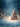 A richly decorated Christmas tree, glowing with warm golden lights and festive ornaments in red, blue, and gold, stands prominently on a shimmering, glitter-covered surface. Delicate white snowflakes fall from a deep blue, soft-focus background filled with warm, golden bokeh lights, creating an enchanting and magical winter wonderland scene.