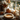 A pumpkin pie decorated with whipped cream sits on a silver platter. Behind it, several pumpkins, pinecones, a candle in a jar, and a vase with flowers and leaves are arranged on a white windowsill in front of a window. The lighting is soft and natural, creating a warm, autumnal ambiance.