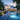 A wide shot of a luxurious, modern white house at twilight, showcasing its illuminated exterior and swimming pool. The house features large glass windows that reveal warm interior lighting, while a long, glowing blue swimming pool stretches in the foreground. Meticulously landscaped gardens, complete with lush trees, bushes, and a vibrant purple flowering tree, are bathed in warm-toned landscape lighting, creating a tranquil and inviting atmosphere.