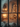A serene indoor Christmas scene viewed through a frosted window pane, creating a blurry foreground effect. Inside, a brightly lit Christmas tree with golden lights and ornaments stands beside a cozy fireplace with a roaring fire. Gifts are arranged beneath the tree and near the fireplace, while a snow-dusted garland and wreath adorn the mantelpiece and wall, all illuminated by warm, inviting light.