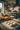 A medium shot of a wooden table in a cozy kitchen, on which six balls of dough covered in flour sit arranged in rows.  A wooden rolling pin lies to the right of the dough, and decorative orange and white pumpkins are arranged on a wooden cutting board in the background. The backdrop is a blurred kitchen with black cabinets and wooden shelves.