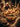 A warm, inviting close-up shot of a holiday dinner table, centered on a golden-brown roasted chicken garnished with rosemary and roasted potatoes. The rustic wooden table is adorned with numerous lit candles, glasses of white wine, and various side dishes. In the blurred background, several people, including elderly individuals, are visible, suggesting a family or friends gathering for a festive meal.