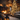 A vertical shot of a beautifully decorated rustic living room during Christmas. A grand stone fireplace with a roaring fire and garland-adorned mantelpiece is on the left, balancing a tall, heavily lit Christmas tree on the right, adorned with various ornaments. The room features exposed wooden beams, a comfortable sofa, and numerous glowing candles in lanterns and on surfaces, casting a warm, festive glow over the patterned rug and wooden floors.