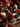 A close-up of a glass jar filled with bright red cranberry sauce, sitting on a dark wood coaster. The scene includes a small white pumpkin, bowls of cranberries and black currants, dried leaves, and a burning candle, all set on a dark wooden surface with a textured beige cloth. The backdrop features blurred flowers and a silver-colored decorative sphere, contributing to a warm and festive autumn ambiance.