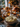 A close-up shot of a Thanksgiving dinner table. In the foreground, a bowl of mashed potatoes topped with herbs sits on a wooden table next to a gray linen cloth. In the blurred background are a roasted turkey, other dishes, gourds, and lit candles, all contributing to a warm and inviting festive atmosphere.