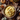 Overhead shot of a beige bowl filled with creamy yellow mashed potatoes, topped with a sprig of thyme and flecks of pepper. The bowl sits on a wooden surface covered with burlap and surrounded by small pumpkins, fall leaves, colorful autumn flowers, vintage silverware, and a decorative pine cone. The scene evokes a cozy, rustic Thanksgiving or autumn harvest celebration.