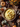 Overhead shot of a beige bowl filled with creamy yellow mashed potatoes, topped with a sprig of thyme and flecks of pepper. The bowl sits on a wooden surface covered with burlap and surrounded by small pumpkins, fall leaves, colorful autumn flowers, vintage silverware, and a decorative pine cone. The scene evokes a cozy, rustic Thanksgiving or autumn harvest celebration.