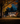 A two-story house is shown at dusk. The house is white with a dark roof and black shutters, with warm light emanating from the windows. The front yard is green, with a scattering of fallen autumn leaves, and several orange pumpkins sit on the front porch, suggesting fall or Halloween.
