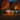 A one-story white house is decorated for Halloween at twilight. Orange, glowing pumpkins line the walkway leading to the front door. The surrounding trees are filled with vibrant orange and red autumn leaves, and the sky is a deep blue.
