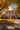 A two-story house is pictured in autumn with golden leaves covering the yard and driveway. The house is light-colored with a brown roof, shutters, and a decorated front door. Pumpkins and other fall decorations adorn the porch, adding to the cozy autumnal atmosphere.