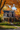 A two-story house is viewed from the street on a sunny day in autumn. The house is decorated with pumpkins and surrounded by trees with vibrant orange and yellow leaves. A gray walkway leads to the front door, creating a welcoming scene.