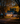 A two-story light blue suburban home is warmly illuminated at twilight, decorated for Halloween. Pumpkins are scattered across the lawn, and the trees are adorned with vibrant golden fall foliage. The house has black shutters, and lights glow from the windows, creating a cozy and inviting atmosphere.