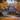 A two-story house is shown during the autumn season. The house is light-colored with a dark roof and black shutters, decorated for fall with pumpkins and gourds. The trees surrounding the house are full of colorful autumn leaves, creating a warm and inviting atmosphere.