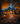 A two-story house is decorated for Halloween at dusk. Carved pumpkins with lights inside line the walkway and are placed along the front of the house. The lawn and pathway are covered in fallen orange and brown leaves, and the house windows are lit from within.