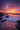 A breathtaking view of a beach at sunset. The sky is filled with vibrant pink and orange clouds, reflecting on the gentle waves. Dark rocks line the shore, creating a dramatic contrast with the colorful sky and the foamy water.