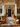 A beautifully decorated front porch greets visitors with autumnal charm. Pumpkins of various sizes line the steps, interspersed with planters overflowing with colorful mums. A black front door with a fall wreath is framed by white columns and a lantern, creating a warm and inviting scene.