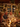 A warm, inviting image of a diverse family or group of friends sharing a joyful holiday dinner around a beautifully decorated table. The scene is illuminated by soft, golden Christmas string lights and glowing candles, with a large, decorated Christmas tree visible in the background. People are laughing and smiling, enjoying food and red wine, conveying a strong sense of togetherness and festive celebration.