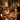 A multi-generational family gathered around a warmly lit dining table, enjoying a festive holiday dinner. A woman in a cream sweater smiles brightly, looking towards the right, while other family members, including an elderly man, laugh and converse. The table is adorned with plates of food, wine glasses filled with red wine, and glowing candles, all contributing to a cozy and joyful atmosphere with blurry golden string lights in the background.