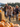 A close-up image shows three children, all smiling and laughing, running towards the viewer at a pumpkin patch, with their father running behind them. In the foreground, many bright orange pumpkins are visible. The scene is bathed in warm, natural light under a partly cloudy sky, with a line of trees visible in the background.